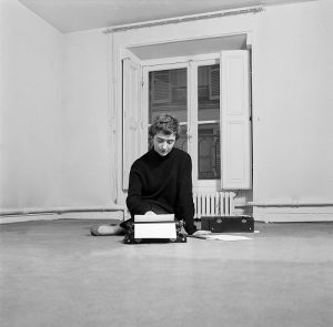 Paris, le 18 février 1956, portrait de l'écrivain Françoise SAGAN dans son appartement de la rue de Grenelle. Elle pose le dos tourné à la fenêtre, assise à même le sol, tapant un texte à la machine