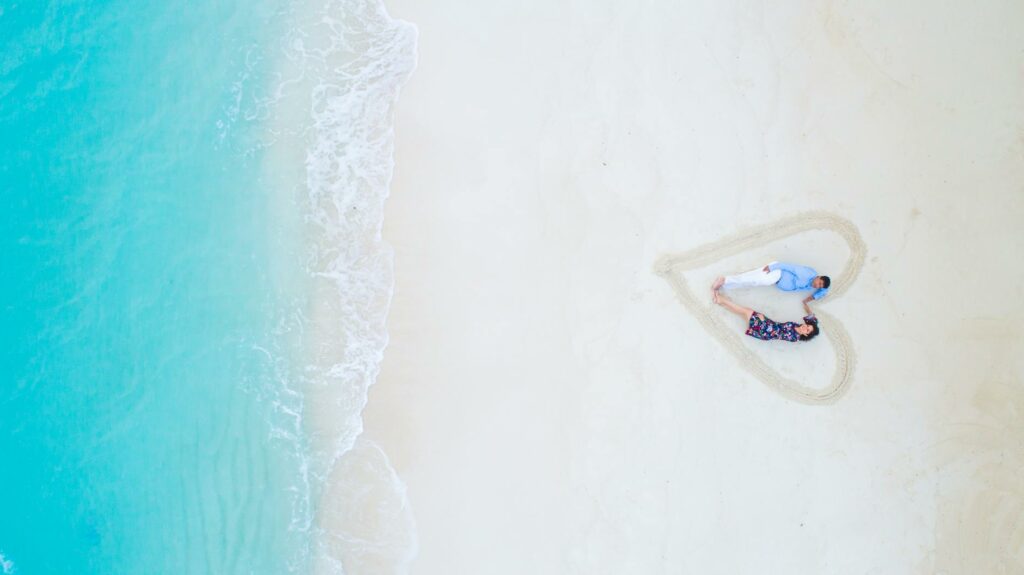 man and woman lying on white sand near sea shore